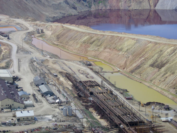 Montana Resources copper precipitation plant adjacent to the Berkeley Pit. A 2013 slough of material from the Pit wall into the water knocked out the 'precip' pump, and precip operations have since ceased. In precipitation, the copper-rich water is pumped over scrap iron, and, in a replacement reaction, the copper solidifies as sludge, while iron takes its place in the water. The water was returned to the Pit by gravity flow, thus not increasing or decreasing the total volume of Pit water. Photo by Justin Ringsak.